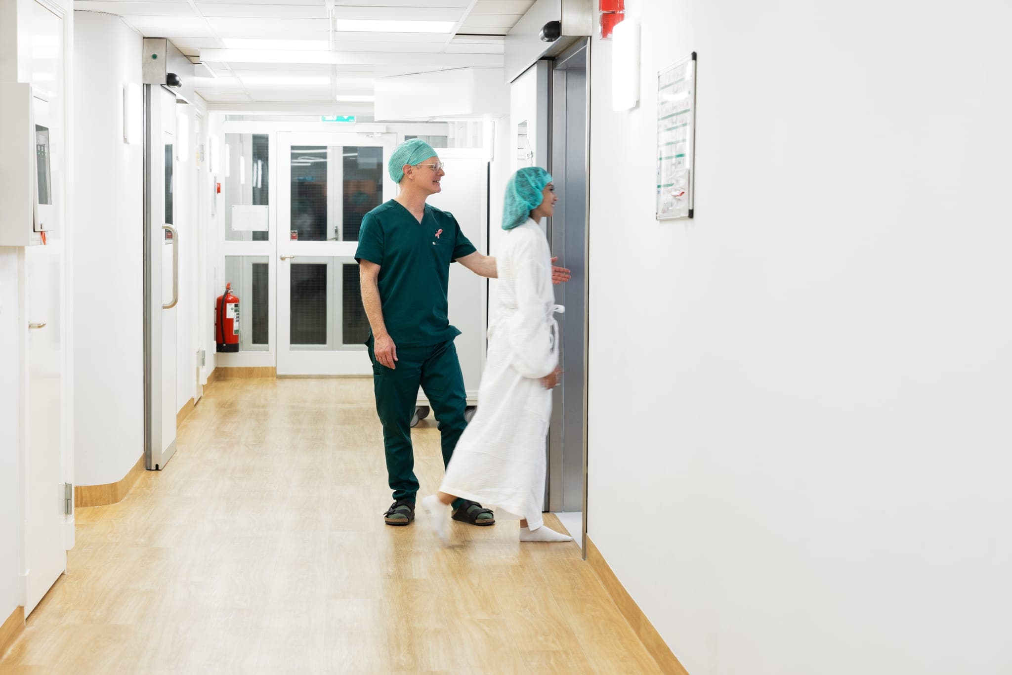 Kirurg följer en patient i morgonrock genom en sjukhuskorridor.