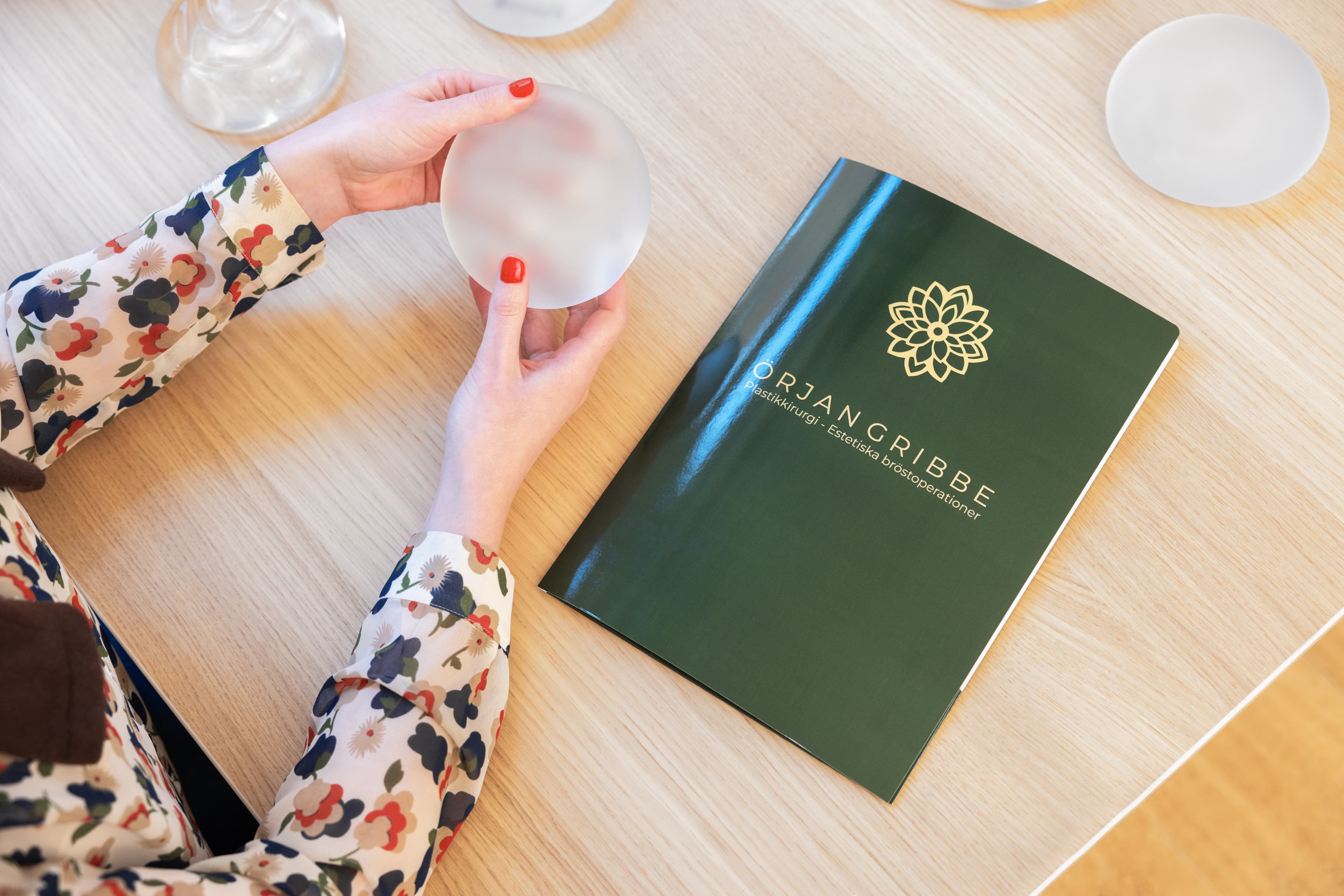 En kirurg i gröna operationskläder visar vägen för en patient klädd i vit morgonrock och grön operationsmössa i en sjukhuskorridor med ljus belysning.